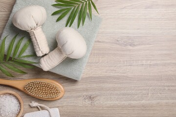 Beautiful spa composition with herbal massage bags and green leaves on light wooden table, flat lay. Space for text