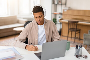 Fototapeta premium Man with headphones writing notes at desk