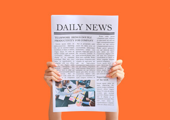 Female hands with newspaper on orange background