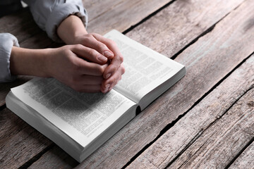Religion. Christian woman praying over Bible at wooden table, closeup