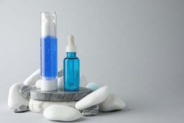 Bottles of cosmetic products and stones on light grey background. Space for text