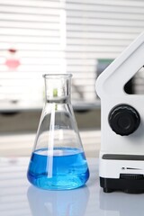 Laboratory analysis. Flask with blue liquid and microscope on white table indoors