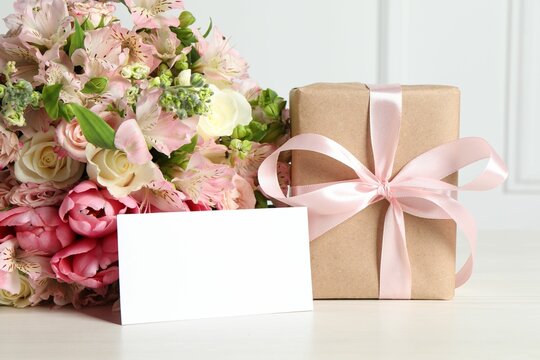 Happy Mother's Day. Gift box, blank card and bouquet of beautiful flowers on white table. Space for text