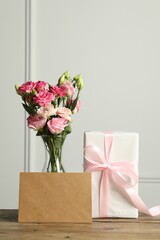 Happy Mother's Day. Gift box, blank card and bouquet of beautiful flowers in vase on wooden table near white wall