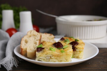 Tasty sausage casserole with green onion and bread on wooden table, closeup