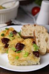 Tasty sausage casserole with green onion and bread on table, closeup