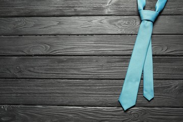 One light blue necktie on black wooden table, top view. Space for text