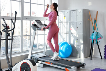 Sporty young woman using inhaler on treadmill in gym