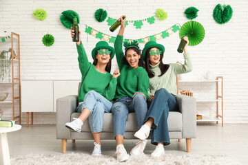 Beautiful young women with bottles of beer on sofa at home. St. Patrick's Day celebration