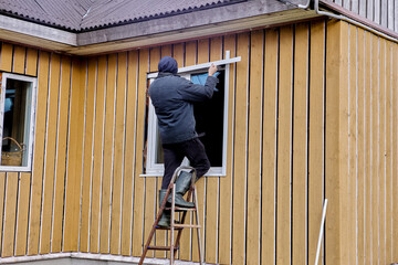 Installation of external metal slopes on window of wooden rural house, outdoor work of construction worker.