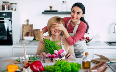 Happy daughter congratulates mom and gives her tulips at home kitchen while she cooking. Birthday, Mothers day, women's day, retired, family, relation, motherhood. - 773485906