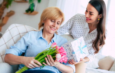 Wonder mother's day. Happy daughter congratulates  mom and gives her flowers and gift at home. Birthday, Mothers day, women's day, retired, family, relation, motherhood. - 773485934