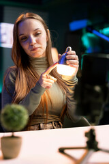Influencer in neon lit studio filming review of light bulb using smartphone on tripod. Tech guru presents smart home automation technology controlled by voice commands, recording with mobile phone