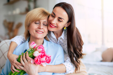 Tender hugs. Happy mature woman with flowers enjoying in daughter's affection on Mother's day. Birthday, Mothers day, women's day, retired, family, relation, motherhood. - 773485974