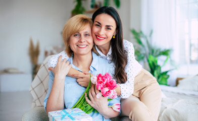 Strong hugs. Lovely daughter embracing her smiling mom with tulips bouquet and looking on camera. Birthday, Mothers day, women's day, retired, family, relation, motherhood. - 773485979