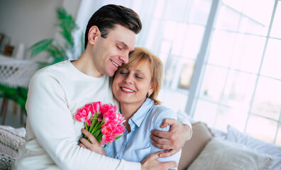 Close up photo of smiling son embracing his cute mother at home with bouquet of tulips. Birthday, Mother's day, women day, retired. - 773486147
