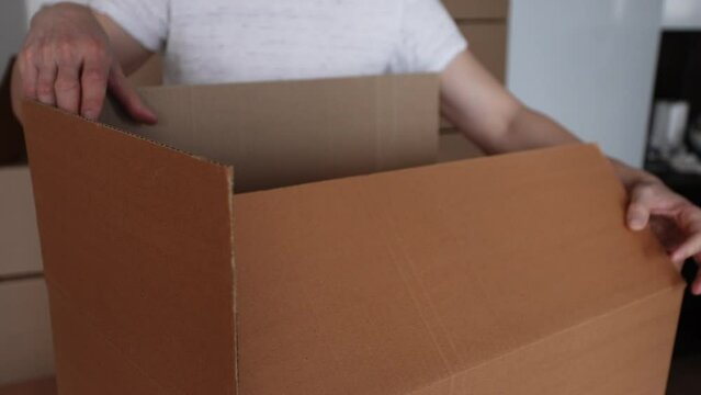 Close-up cropped shot of unrecognizable man packing big cardboard box for personal stuff storing at relocation day, leaves to new own or rented house, prepare dwelling for remodeling or removal work.