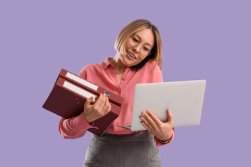 Overwhelmed mature businesswoman with laptop and folders talking by phone on lilac background....