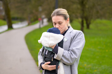 Happy woman kissing her baby that she is holding and carrying in a baby carrier