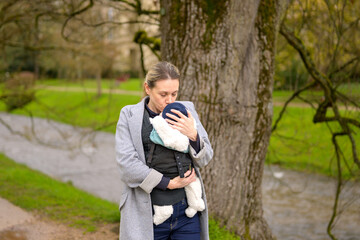 Happy woman kissing her baby that she is holding and carrying in a baby carrier