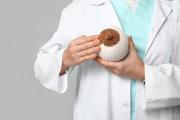 Mature female doctor with knitted model of breast on grey background, closeup. Breast feeding concept