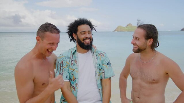 Two young fair-haired shirtless Caucasian friends and dark-haired African American with beard and kinky hair in Hawaiian shirt, ocean in the background. High quality 4k footage