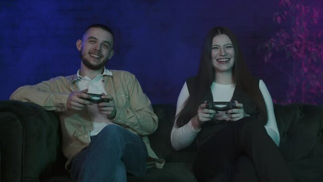 Favorite activity for young people is video games. Brother and sister sitting on couch at home and focused on playstation over smoke background. Boyfriend and girlfriend hold joysticks during