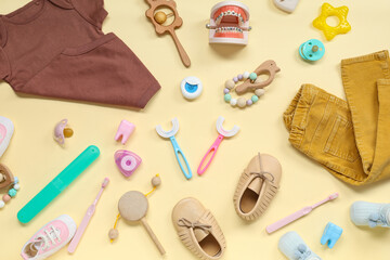 Baby clothes with toothbrushes, jaw model and toys on beige background