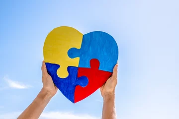 Poster World autism awareness day, Autism spectrum disorder concept. Adult and child hands holding together colorful painted puzzle heart on blue sky background © vejaa
