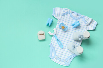Baby clothes with toothbrush, pacifier and dental floss on turquoise background