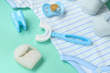 Baby clothes with toothbrush, pacifier and dental floss on turquoise background