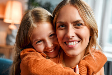Concept of careless childhood. Small girl embracing happy millennial mom during warm family moment