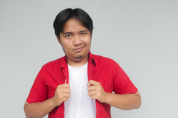 Portrait of a young Asian man in a red shirt with a cocky expression. Isolated in gray background.