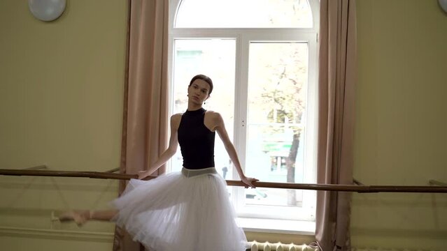 A ballerina trains at the ballet barre in front of a large window