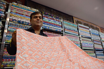 Indian seller showing textiles with variety of colors in shop of a local market
