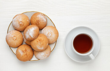 Round-shaped pastry, sprinkled with powdered sugar, on a plate and a cup of tea. view from above