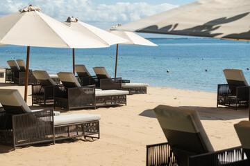 Beach beds with umbrellas, on the ocean coastline, on the hotel grounds among greenery. - obrazy, fototapety, plakaty