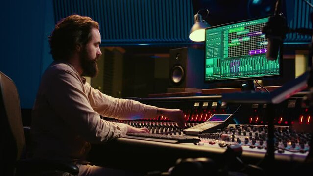 Professional tracking engineer editing music by adding sound effects in control room at studio, recording tracks and using mixing console. Producer operates technical equipment. Camera B.