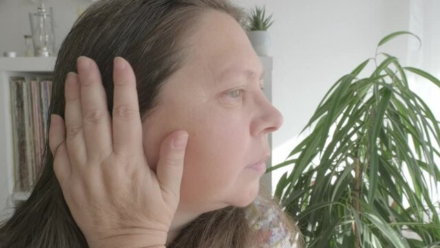 self-aware woman 50 years of age, takes moment to assess her facial features, particularly jowls, reflecting on natural process of aging and considering options for maintaining youthful appearance