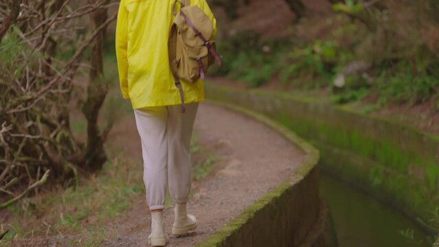 A girl in a yellow jacket travels with a backpack and visits extraordinary places and trails on the island of Madeira, Levada dos Tornos, Portugal