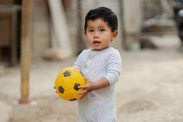 Hispanic little boy playing with a ball in the backyard of his house - Boy spending time outdoors - Latin boy with a ball