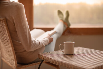 Woman enjoying a hot cup of tea and a book on a cozy winter morning 