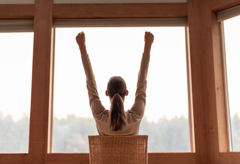 Young joyful woman with arms up looking out her window in the morning  feeling happy and inspired 