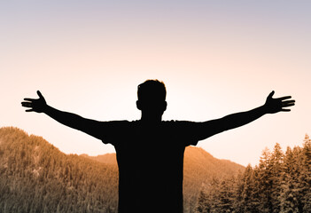 Young man arms outstretched on a mountain at sunrise enjoying freedom and life, people travel...