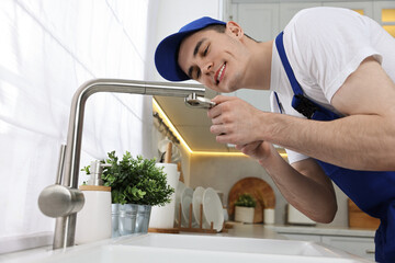 Smiling plumber repairing faucet with spanner in kitchen, low angle view