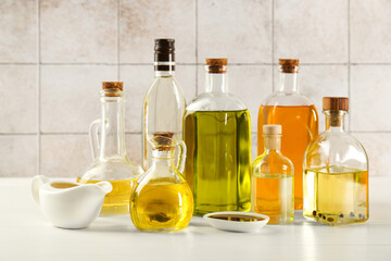 Vegetable fats. Different oils in glass bottles and dishware on white wooden table against tiled wall - obrazy, fototapety, plakaty