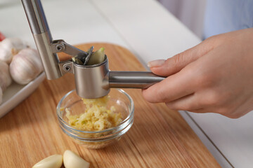 Woman squeezing garlic with press at white table, closeup