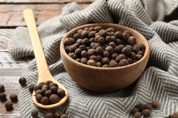 Aromatic allspice pepper grains in bowl and spoon on wooden table