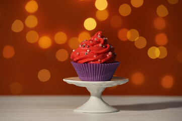 Stand with tasty cupcake on white table against blurred lights