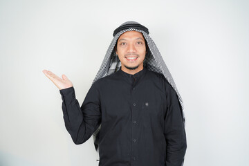 Cheerful Asian Muslim man wearing Arab turban sorban pointing hand finger at empty space on isolated